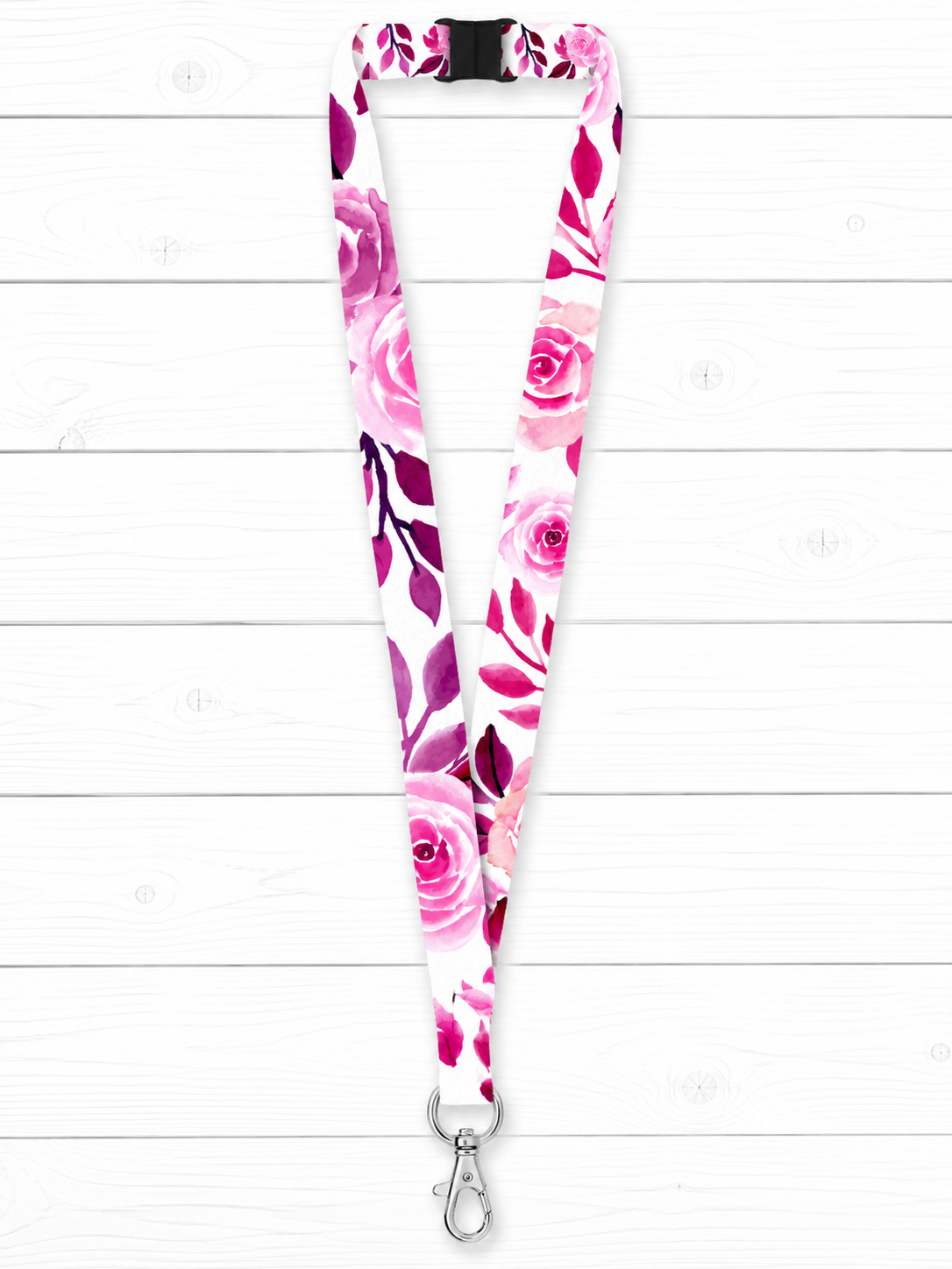 A floral print lanyard with a white background and pink, magenta, and purple rose pattern, featuring a black plastic buckle at the top and a silver metal swivel clasp at the bottom, displayed against a white wood plank background.