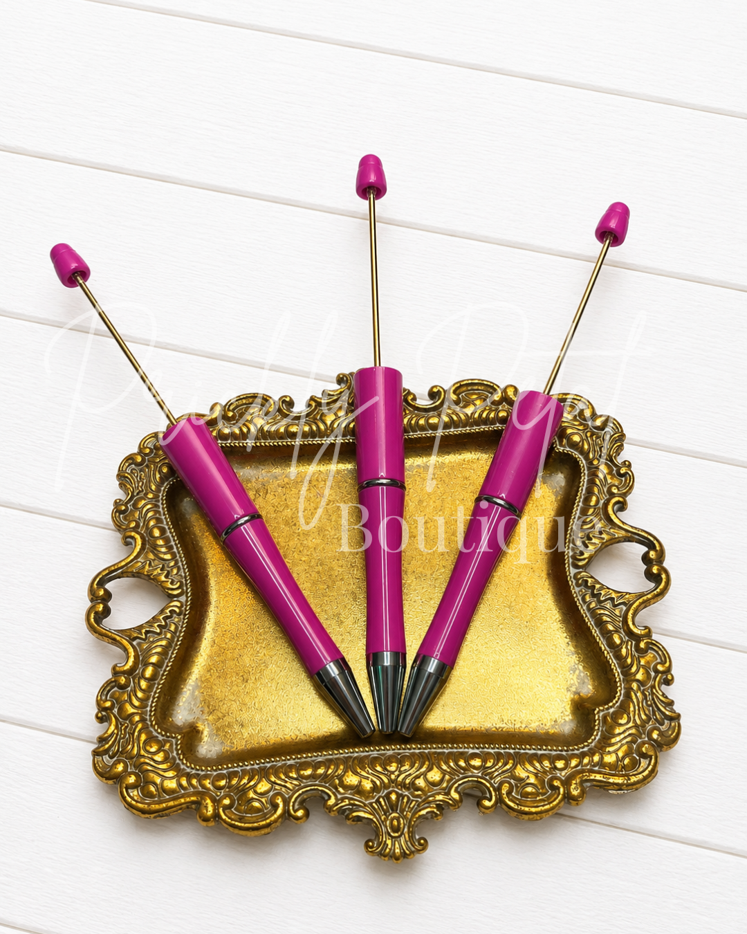 fuschia beadable pen on gold tray against white wood