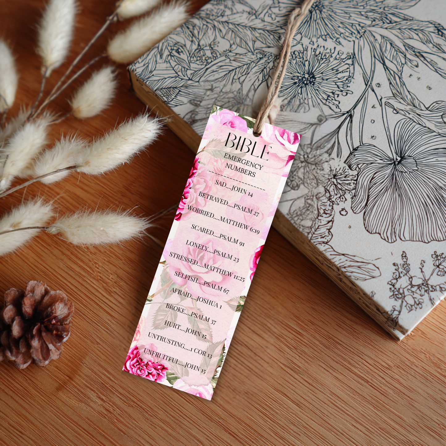 Floral bookmark with Bible emergency numbers on a wooden surface with a book and decorative elements.