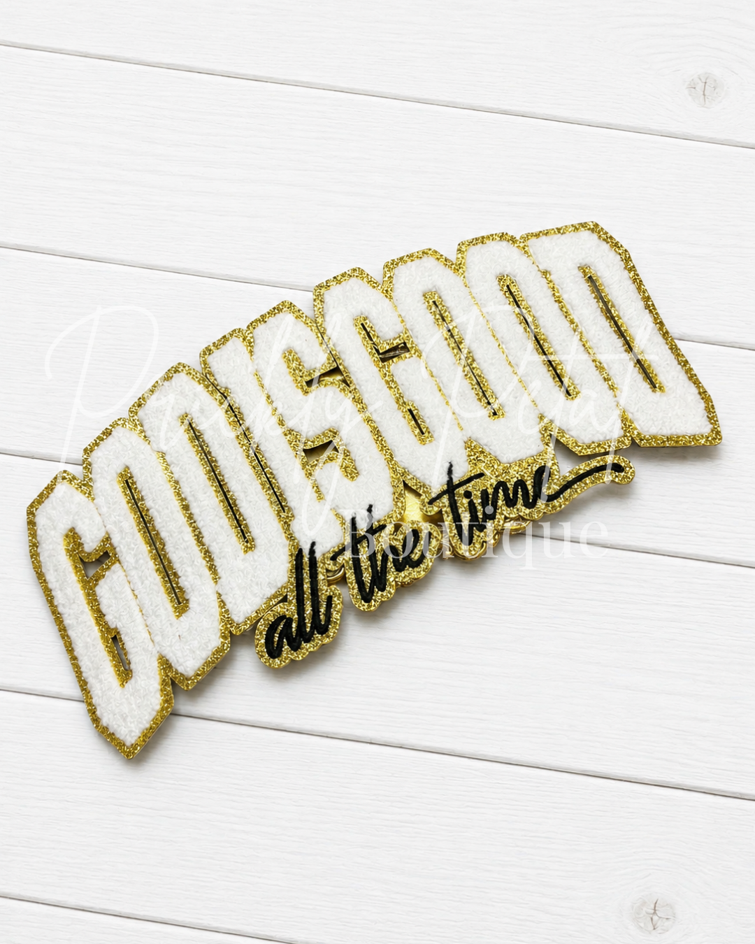 A die-cut embroidered patch with the words 'GOOD all the time' in white fuzzy letters outlined in glittery gold, with 'all the time' in black script on a white wood plank background.