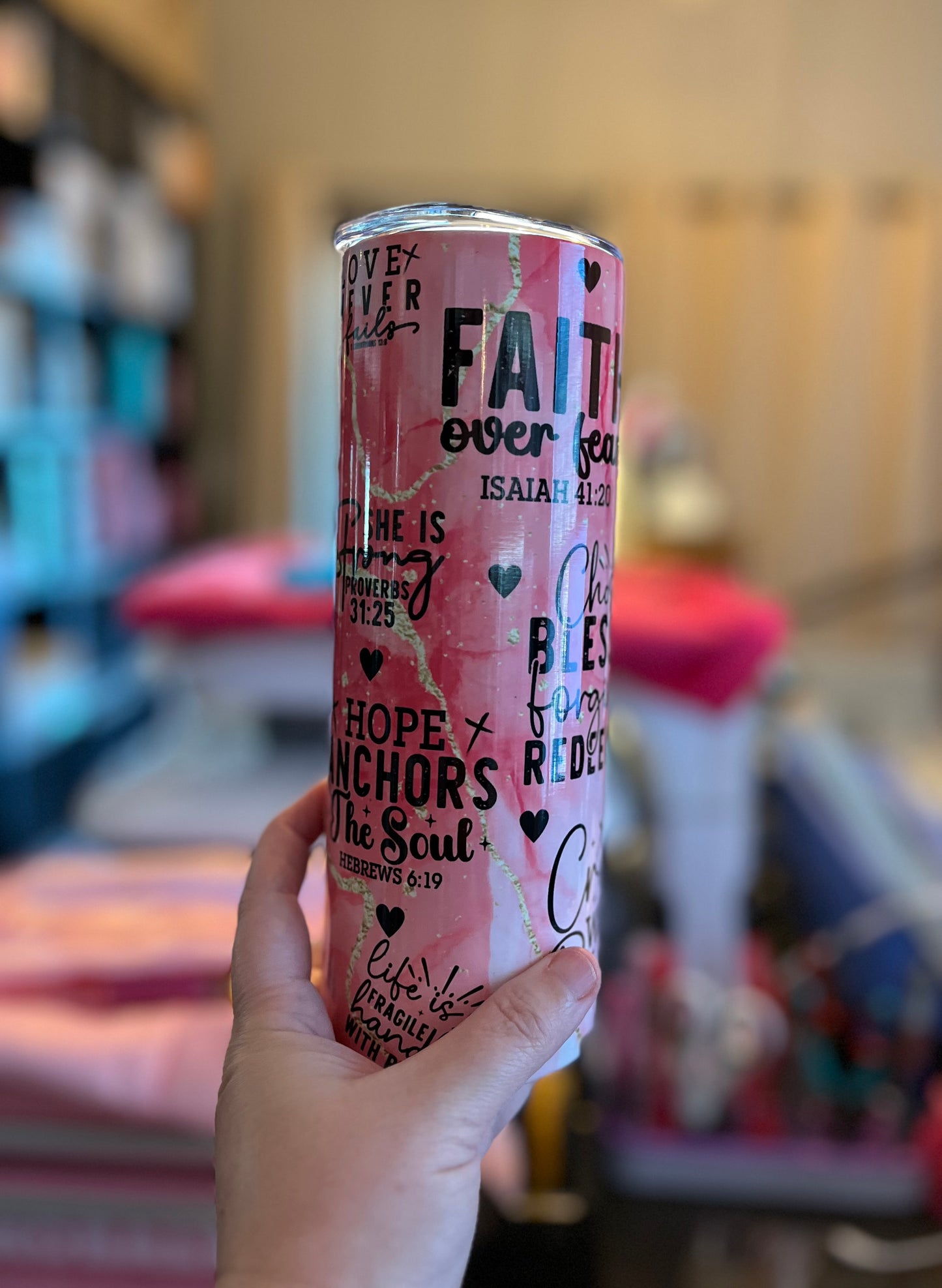 Pink tumbler with motivational text held in a hand against a blurred indoor background