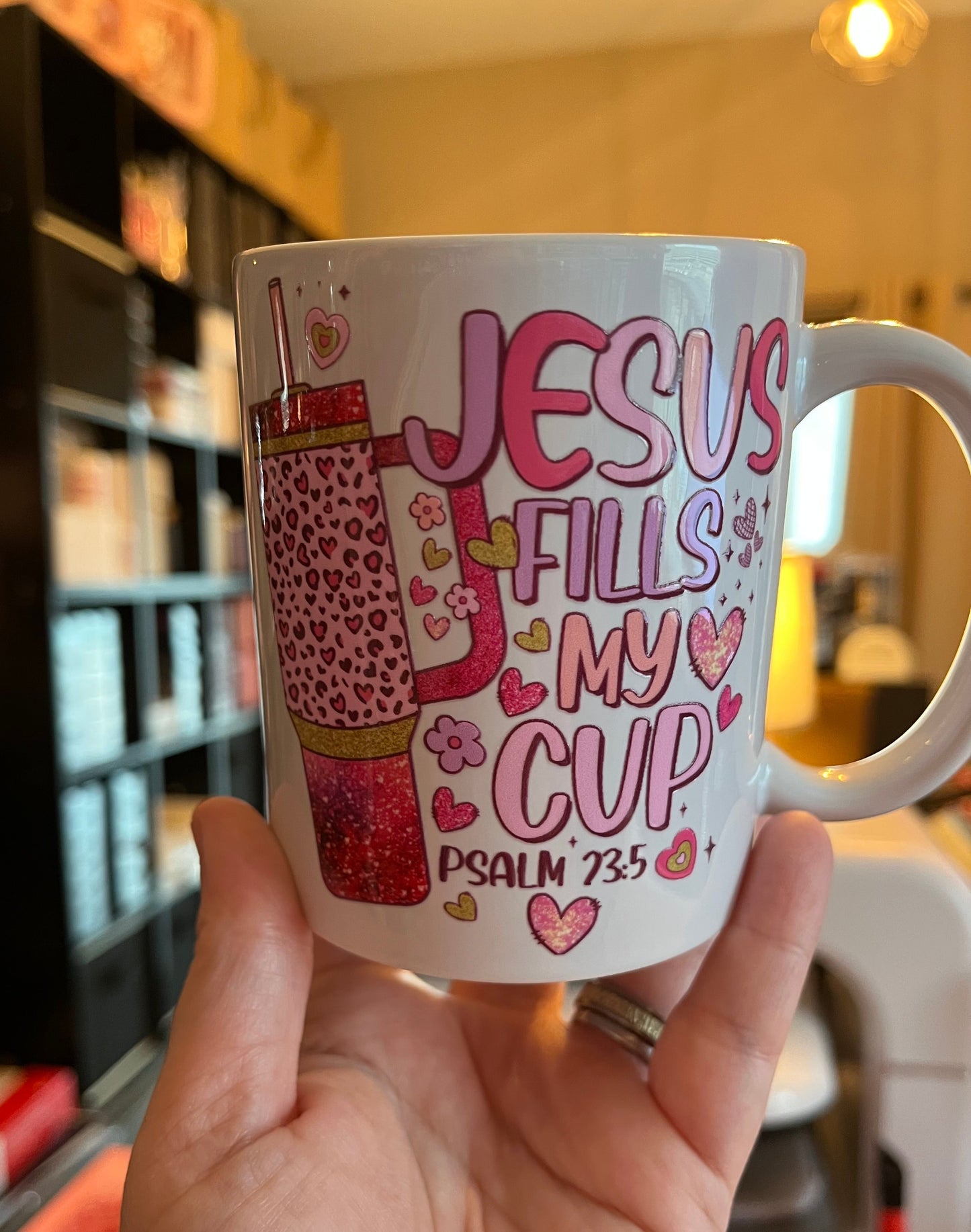 White mug with pink text and design held by a hand, blurred background