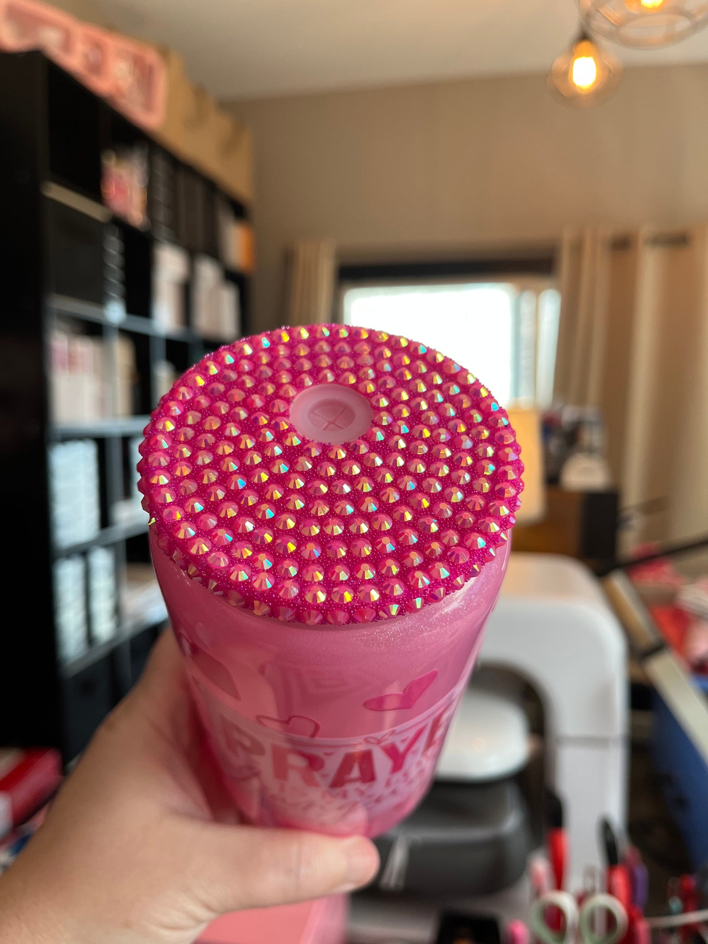 Pink blinged-out bottle held in a hand with a blurred indoor background