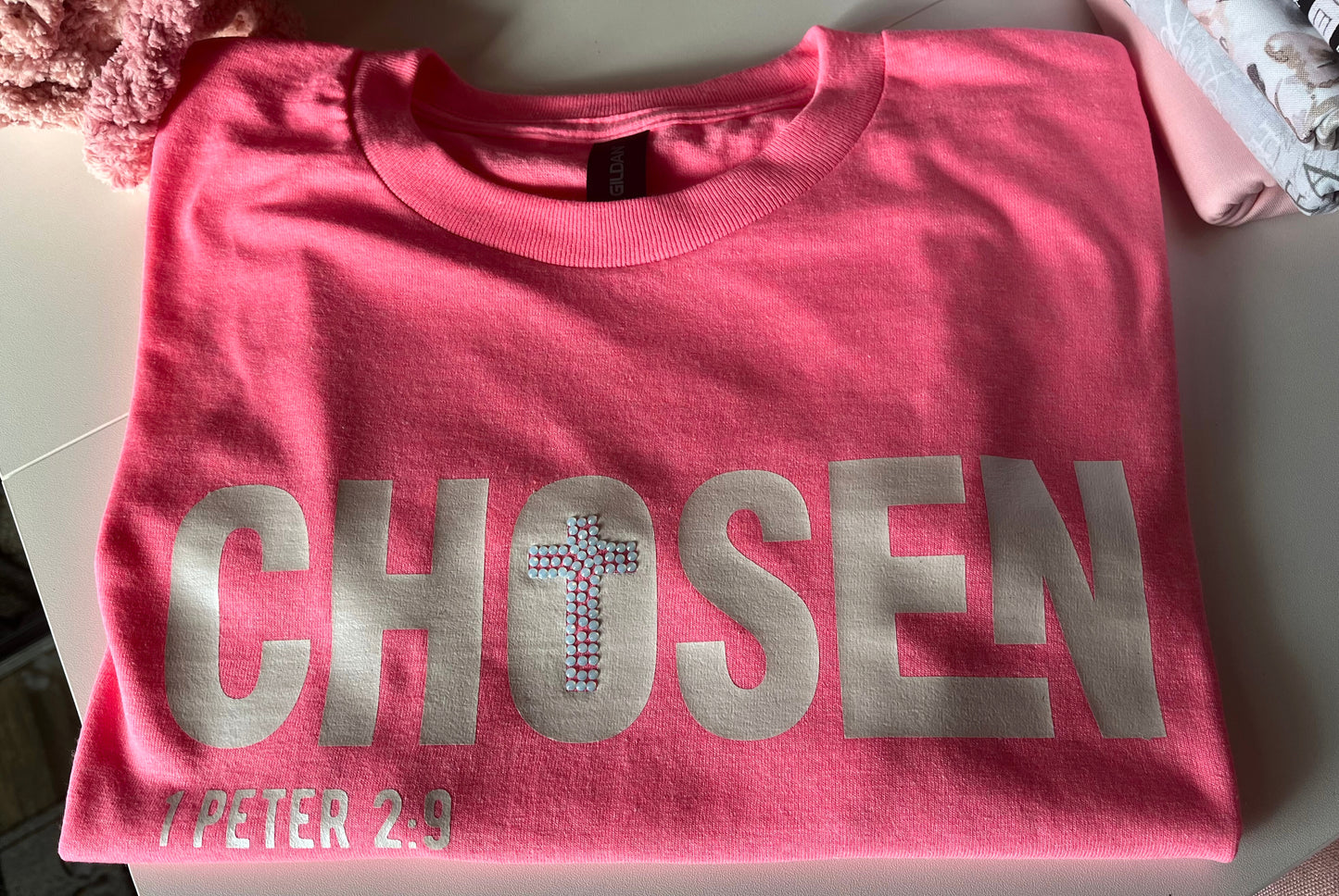Pink t-shirt with 'CHosen' text on a white surface