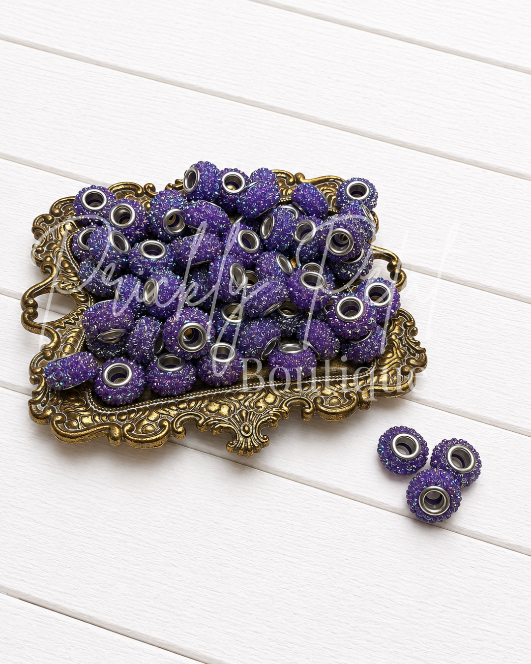 Purple glitter spacer beads with silver-toned metal centers, displayed in an ornate gold tray on a white wood background.