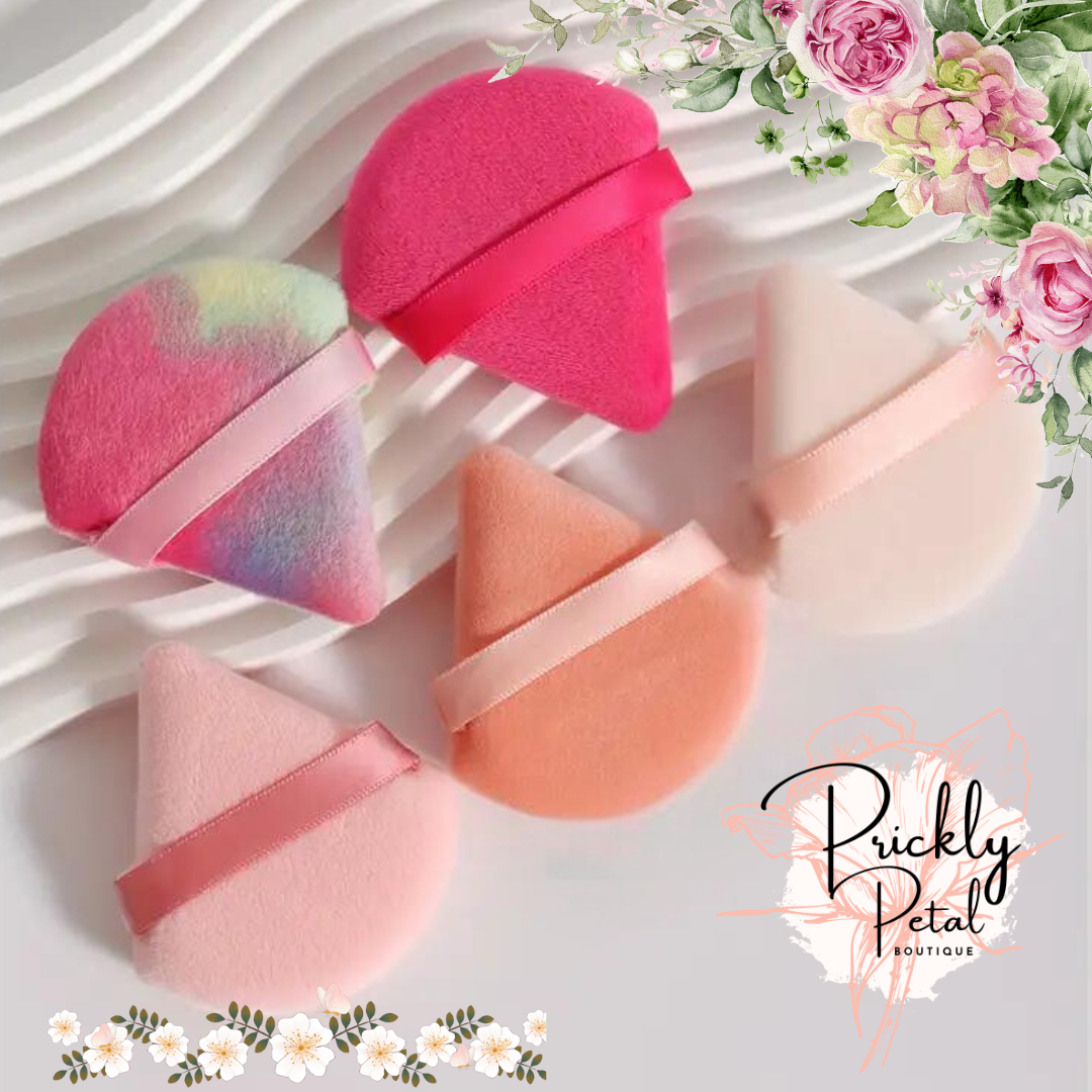 A set of triangular-shaped makeup sponges in various shades of pink and orange, displayed on a white surface with floral graphics in the corner.