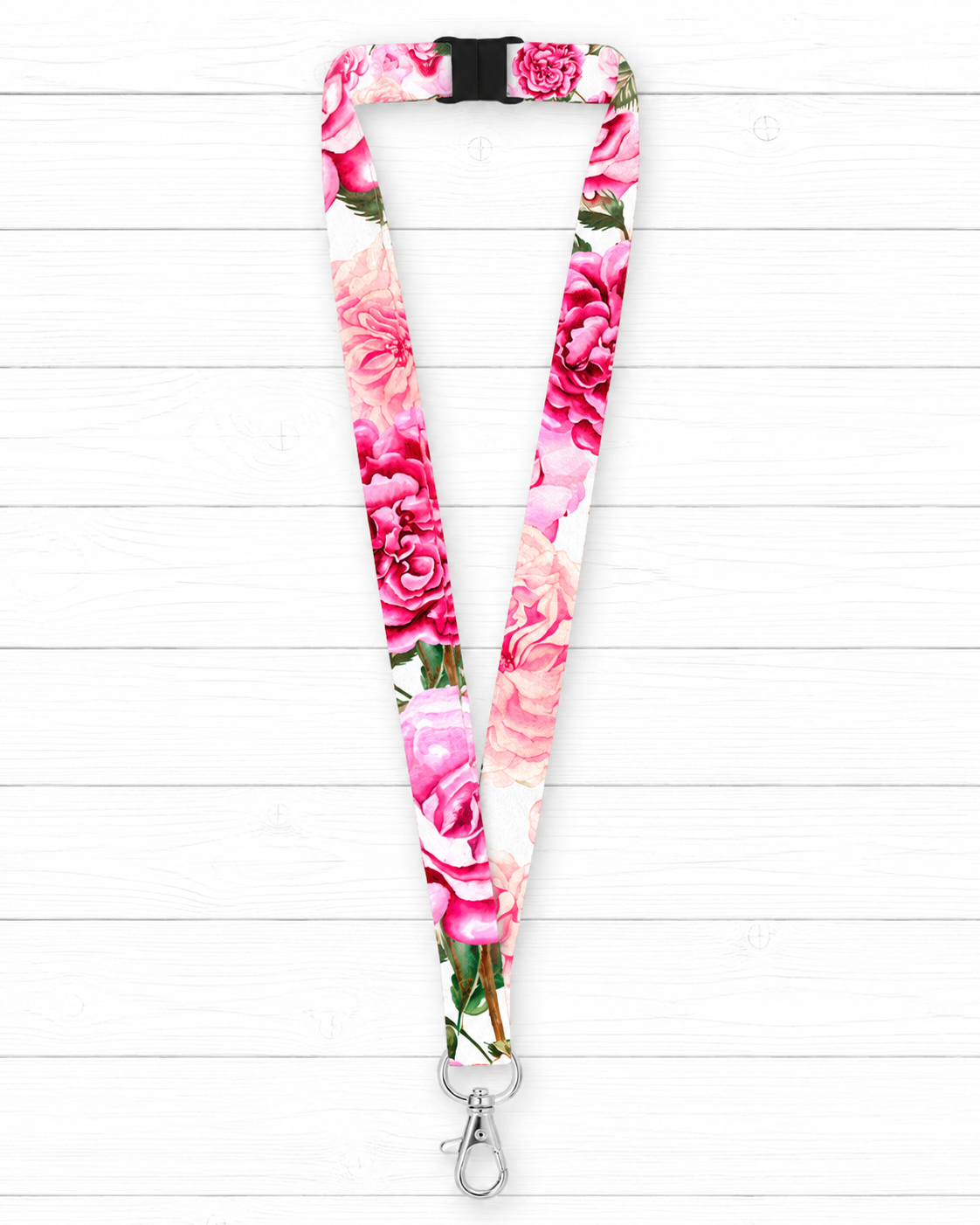 A floral-patterned lanyard with a pink and red rose print on a white background, featuring a black plastic buckle at the top and a silver metal lobster clasp at the bottom, displayed against a white wood plank background.