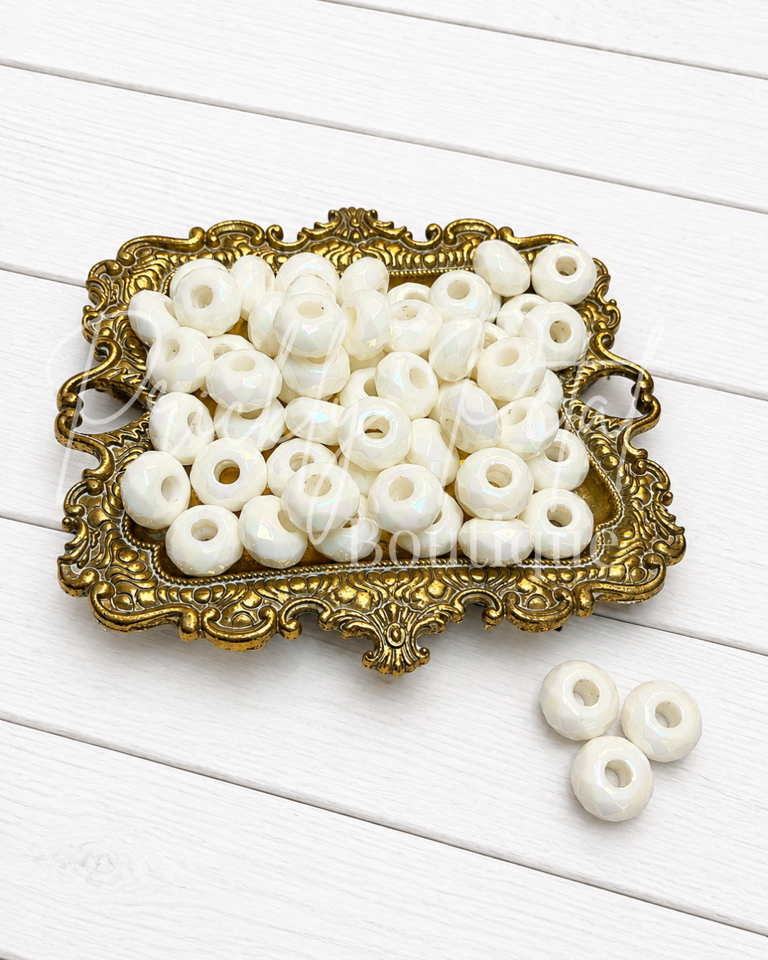 White round beads with center holes, displayed in an ornate gold tray on a white wooden background.