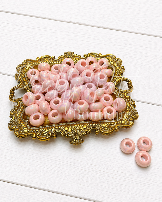 Pink round craft beads with a glossy finish, displayed on an ornate gold tray with three additional beads on the side, set against a white wooden background.