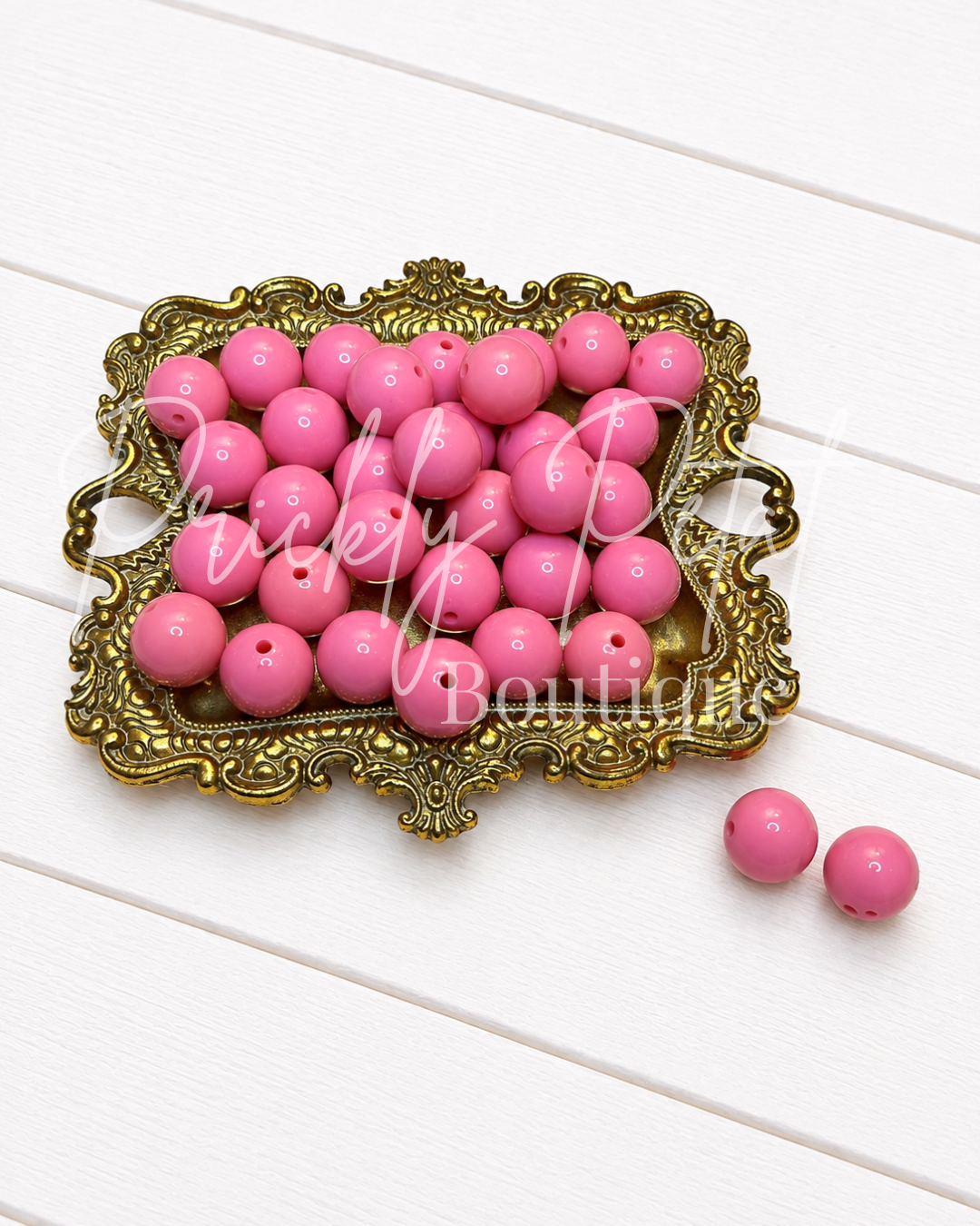 pink acrylic round beads on gold tray against white wood background