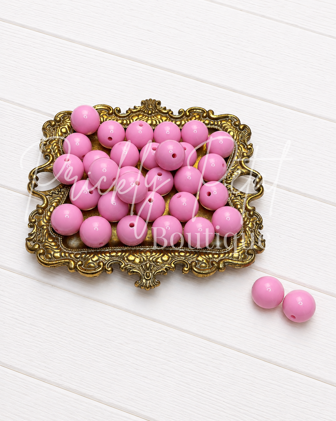 Pink round wooden beads with drilled holes, displayed on an ornate gold tray with two additional beads on a white wood background.