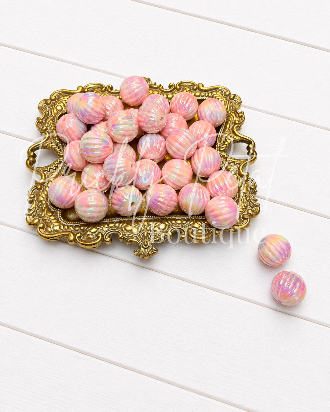 two tone pink bead on gold tray against white wood background