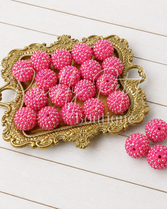 Pink rhinestone-covered round beads threaded on a string, displayed on an ornate gold tray over a white wood plank background.