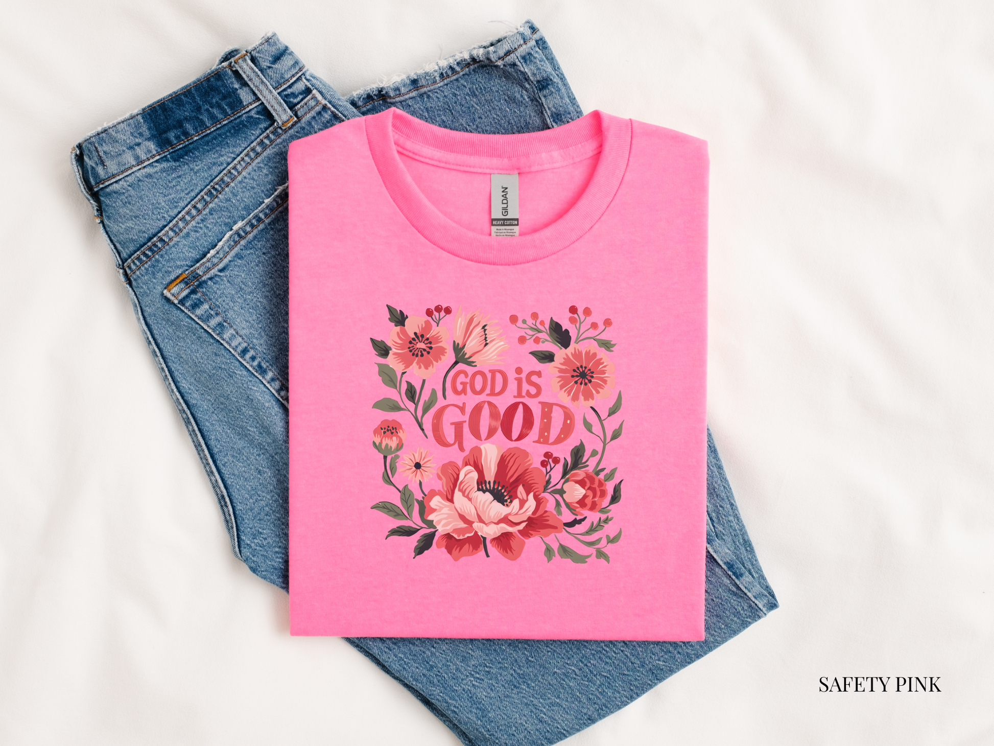 Pink t-shirt with floral design and 'God is Good' text on blue jeans.