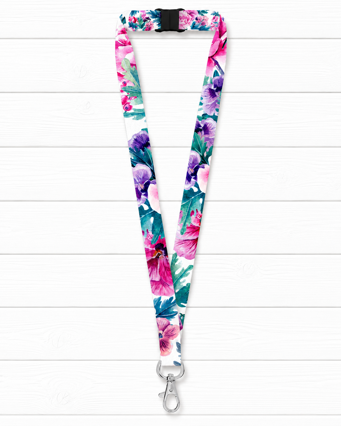 A floral lanyard with a vibrant watercolor print of pink, purple, and teal flowers on a white background, featuring a black plastic buckle at the top and a silver metal swivel clasp at the bottom, displayed flat on a white wood plank background.