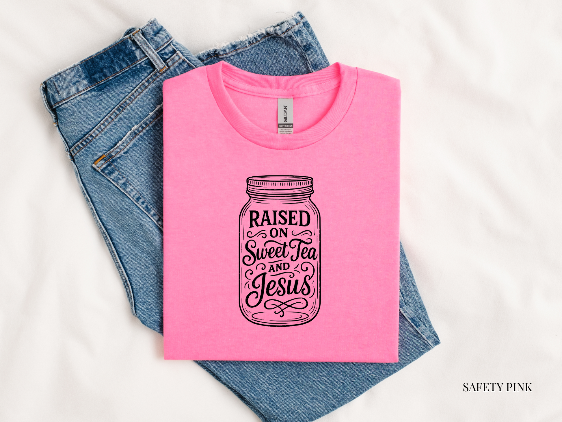 Pink t-shirt with 'Raised on Sweet Tea and Jesus' design on blue jeans