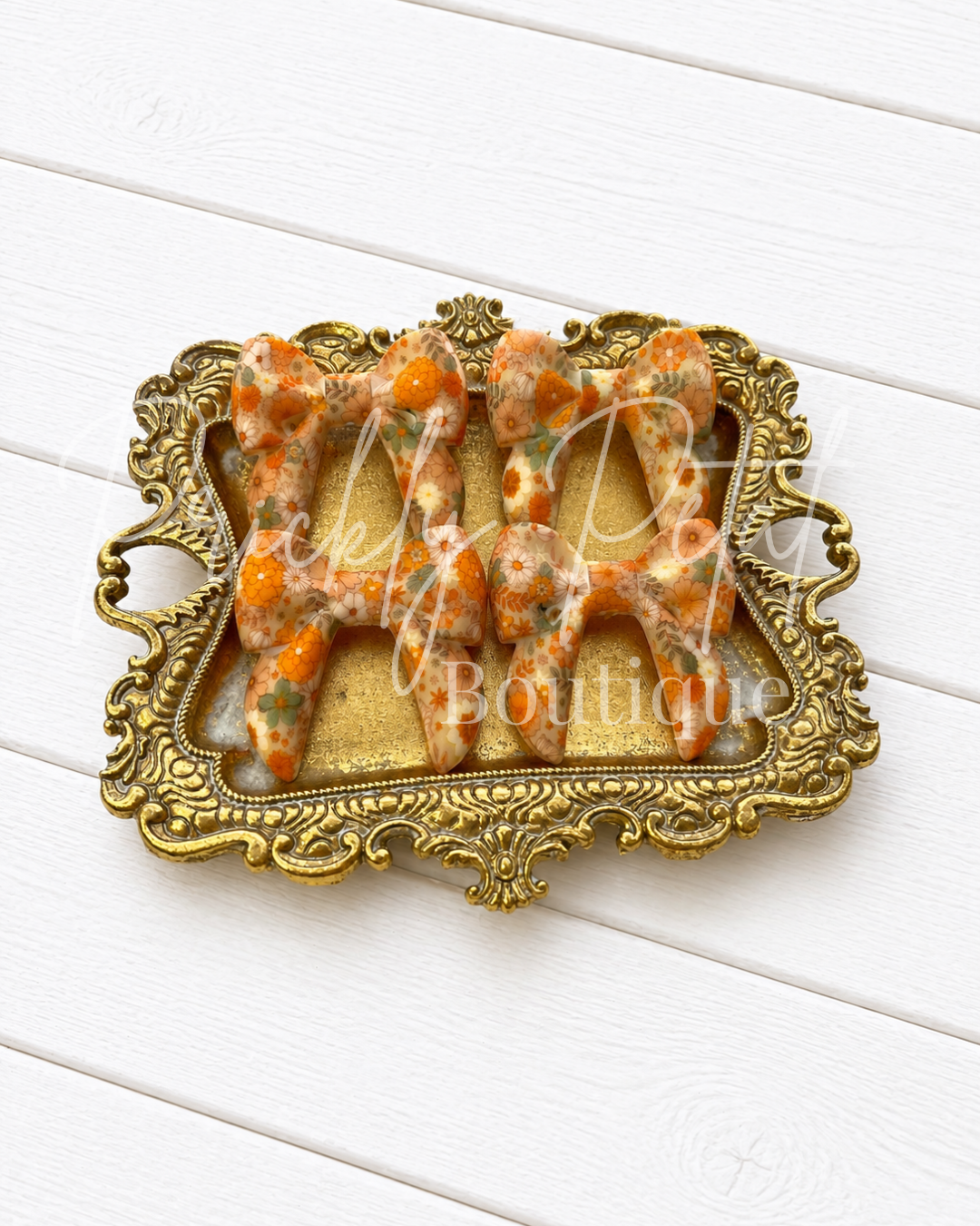Four silicone bows, displayed on an ornate gold tray over a white wood plank background.