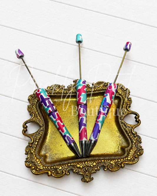 colorful crosses beadable pen on gold tray against a white wood backdrop