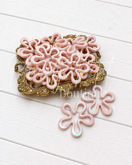 Pink flower-shaped bead on gold tray against white wood background