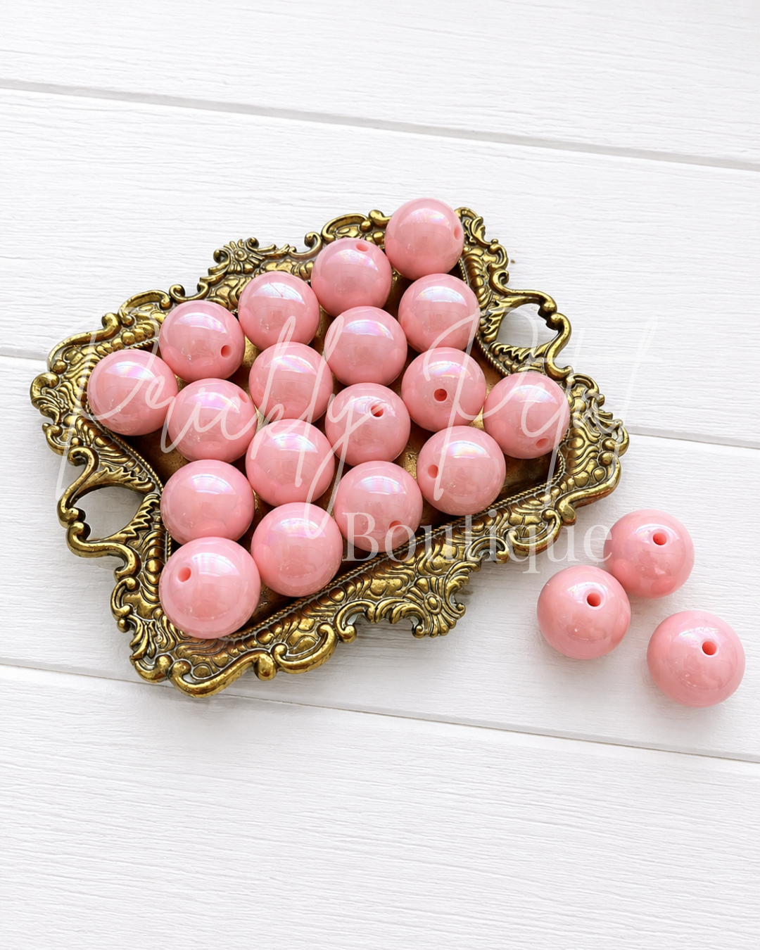 Pink round craft beads with holes, displayed in an ornate gold-colored tray on a white wood background.