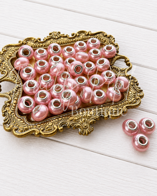 Pink faux pearl spacer beads with silver metal ends, displayed on an ornate gold tray over a white wood background.