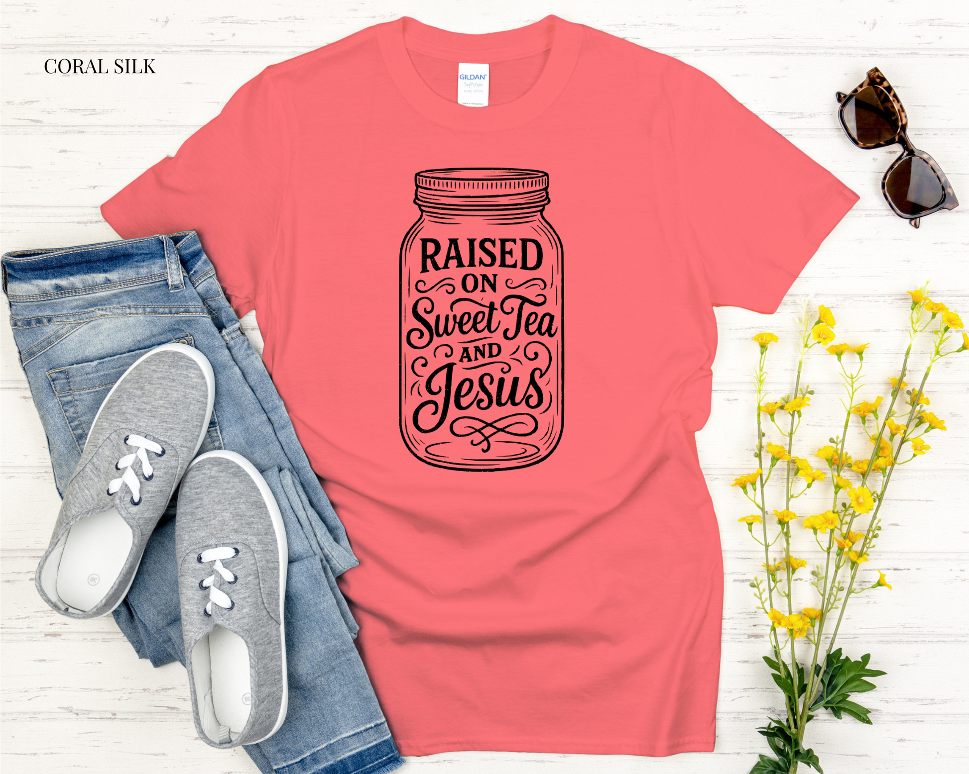 Coral t-shirt with 'Not Today Satan' text, jeans, sneakers, and sunglasses on a light wooden surface.