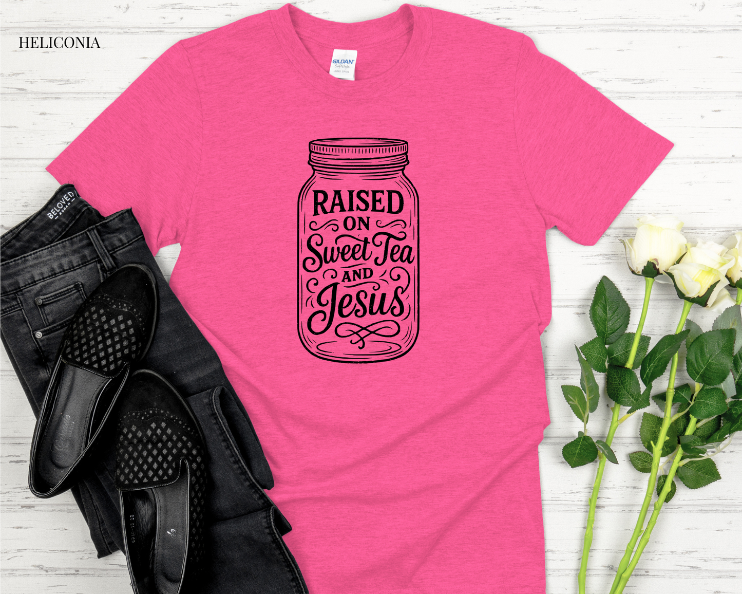 Pink t-shirt with a jar graphic and text on a white surface with black shoes and flowers.