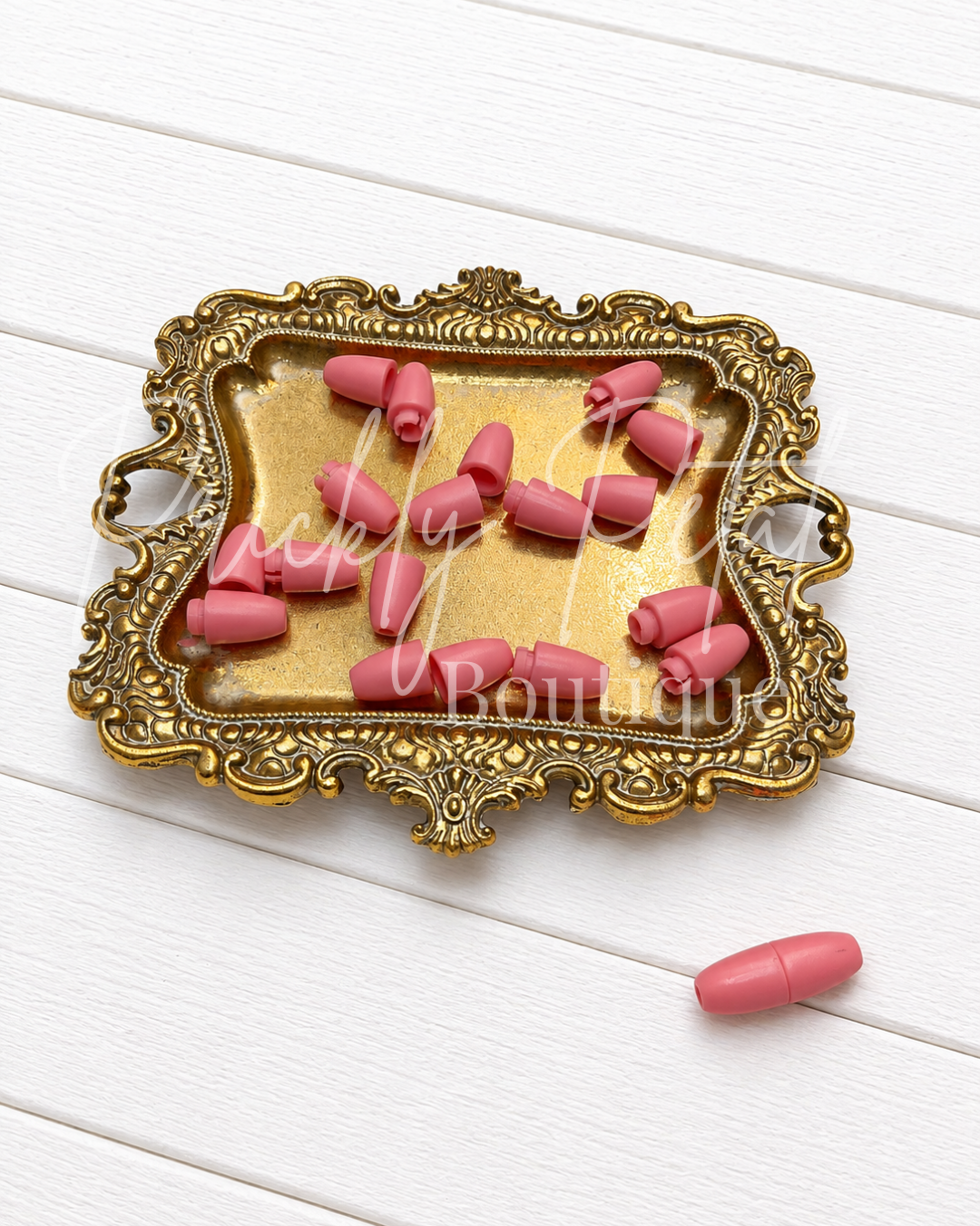 Pink breakaway lanyard clasps arranged on an ornate gold tray, with one clasp placed beside the tray on a white wood background.