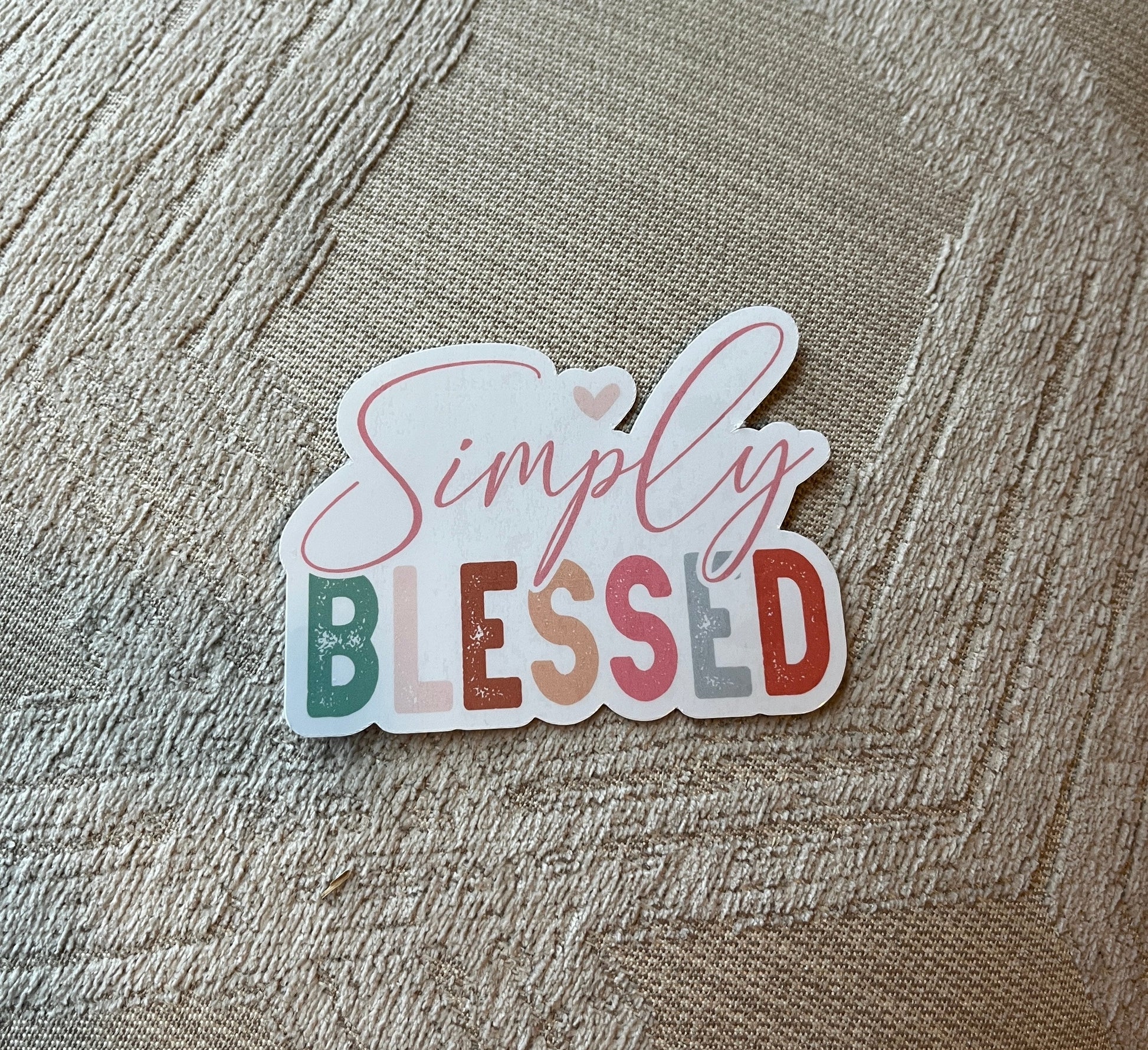 Sticker with 'Simply Blessed' text on a textured fabric background