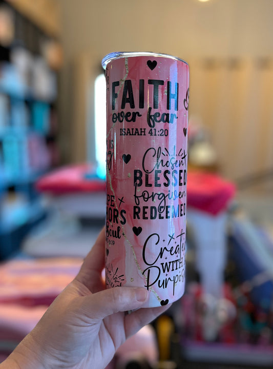 Pink tumbler with motivational text held in a hand against a blurred background
