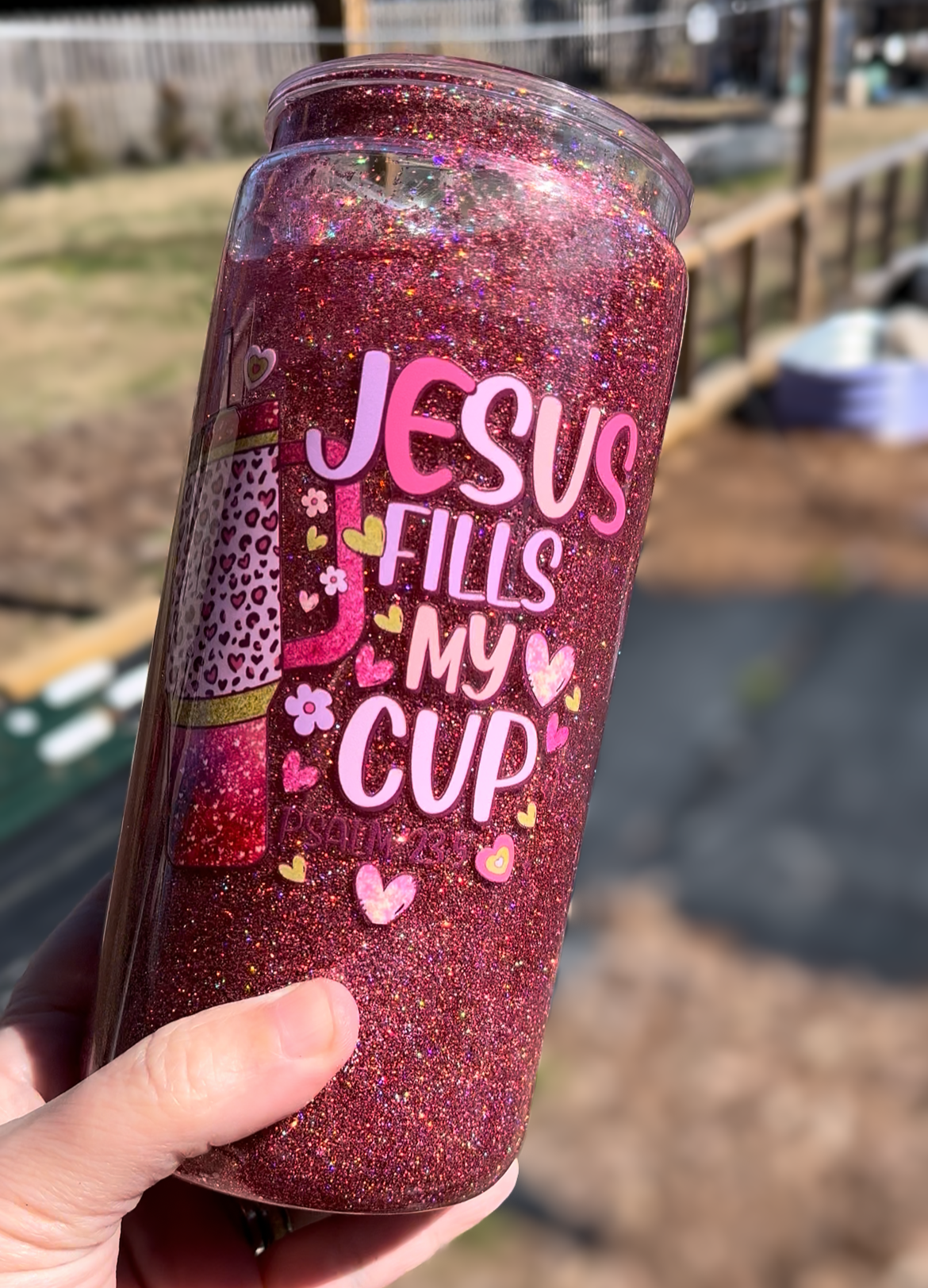 Glittery tumbler with 'Jesus Fills My Cup' text held outdoors.