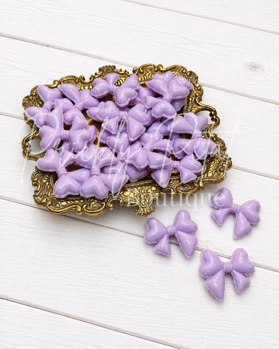 Lavender purple bow embellishments displayed on an ornate gold tray, with three individual bows placed beside it on a white wood plank background.