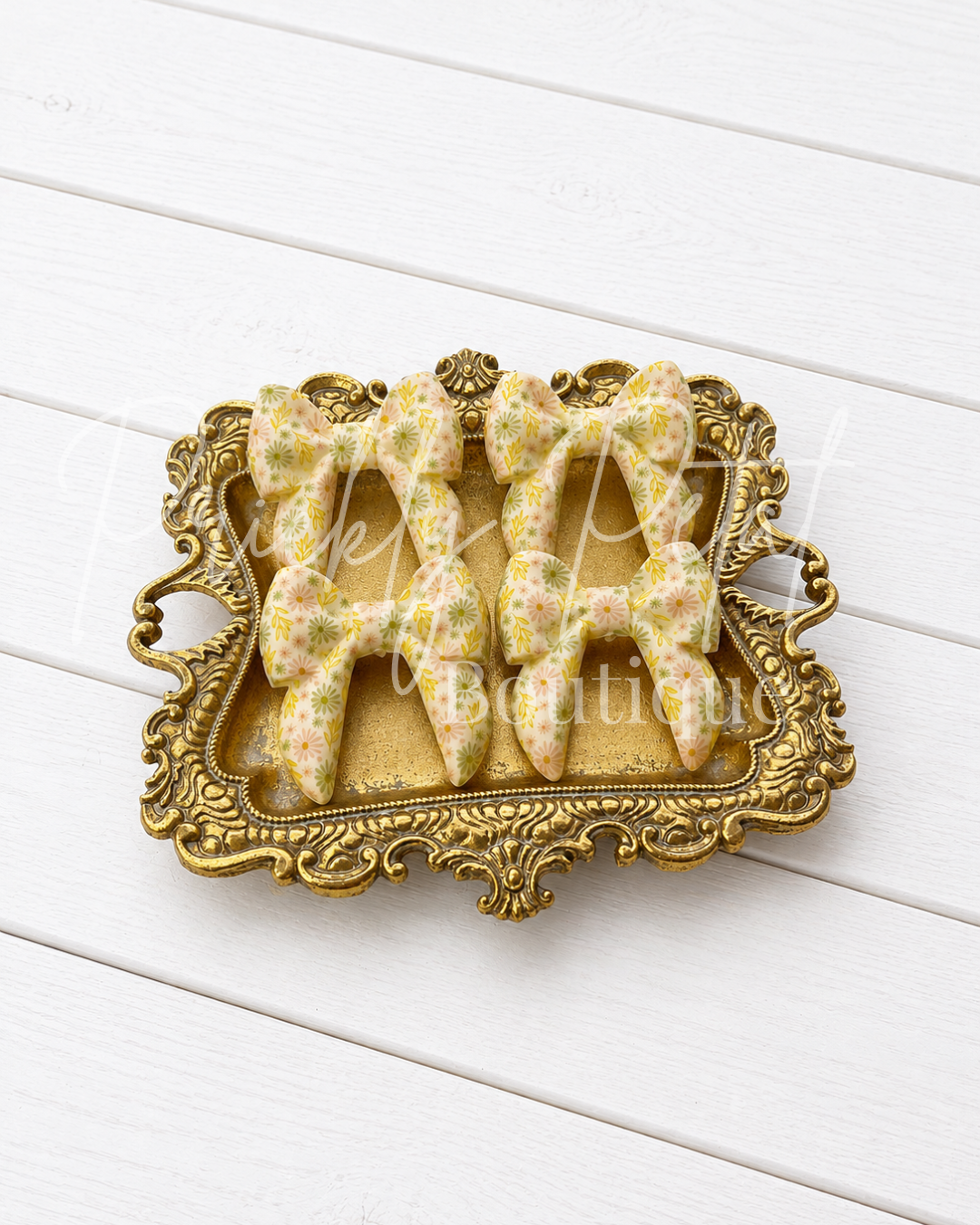 silicone bows displayed on an ornate gold tray over a white wood plank background.