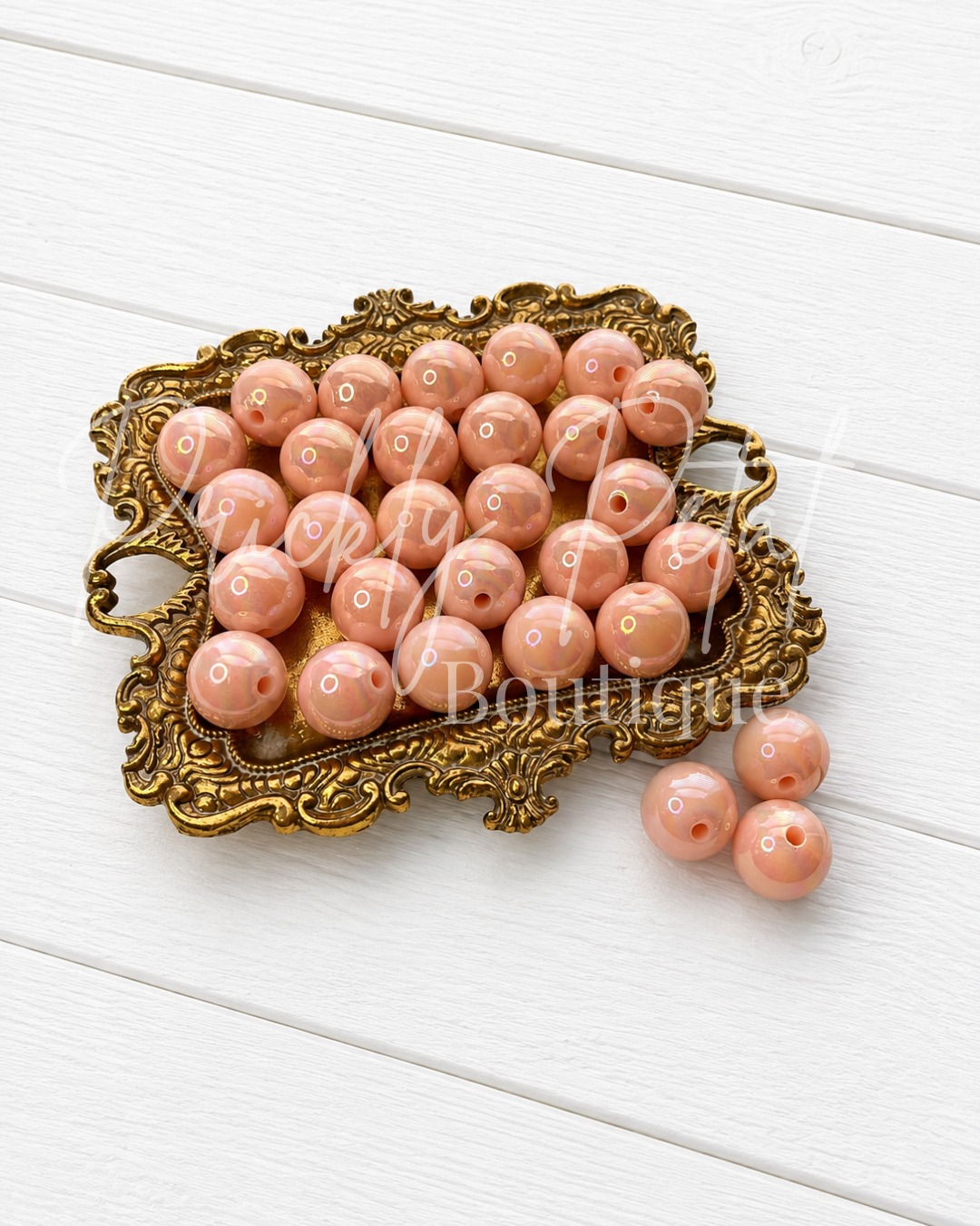Round peach-pink glass beads with white polka dots, displayed on an ornate gold tray with three beads resting beside it on a white wooden background.