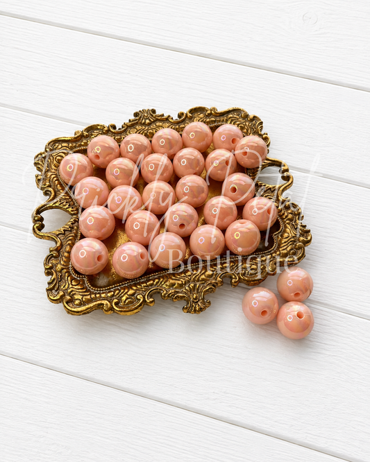 Round peach-pink glass beads with white polka dots, displayed on an ornate gold tray with three beads resting beside it on a white wooden background.