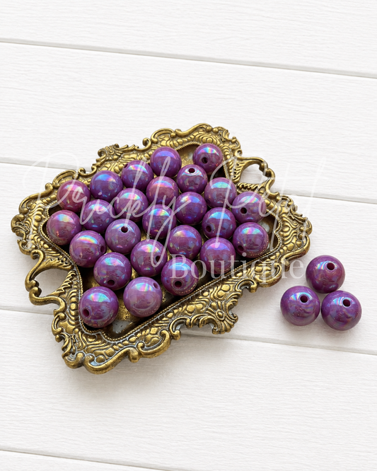 Purple marbled round craft beads with a glossy finish, displayed in an ornate gold-colored metal dish on a white wooden background. Three beads are shown outside the dish to the right.