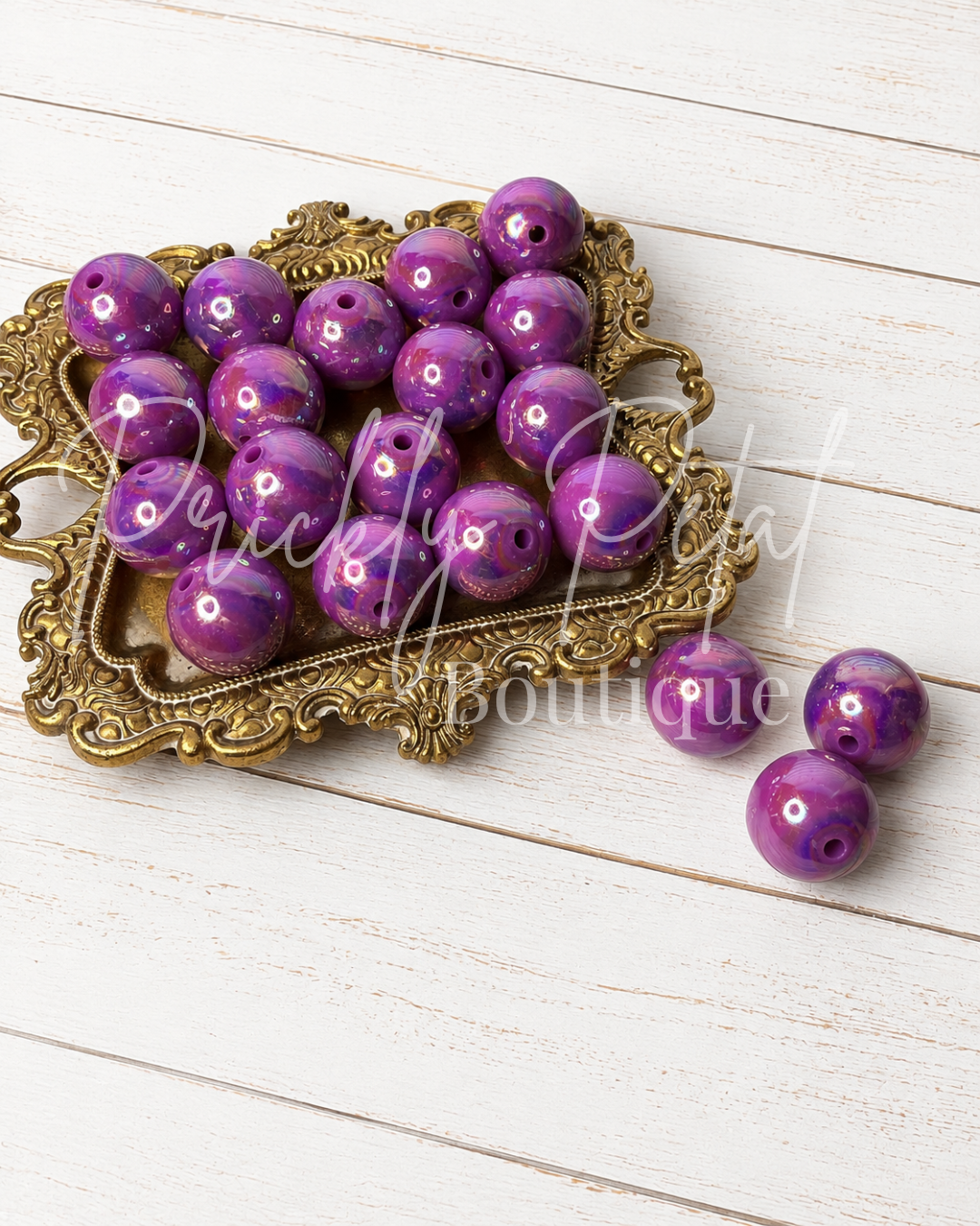 Purple marbled round craft beads with drilled holes, displayed on an ornate gold tray with three additional beads on a white wood background.