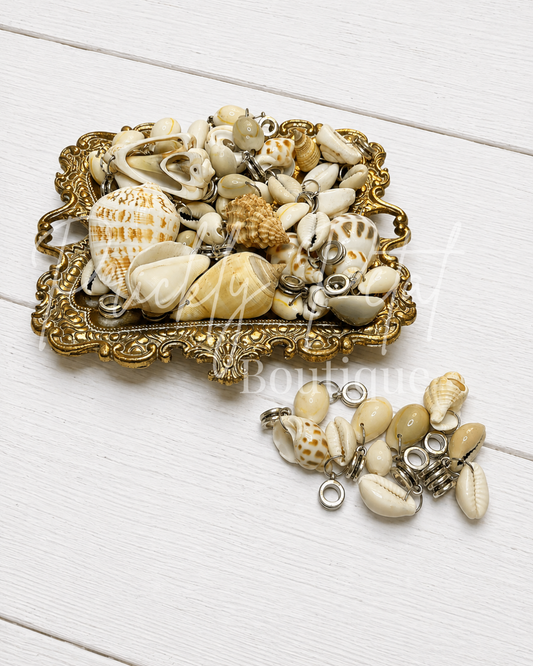 random seashell dangle charm mix on gold tray against white wood background