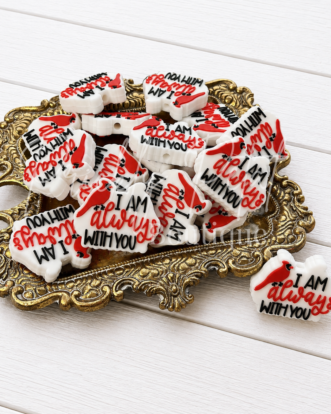 White heart-shaped sugar cookies decorated with red and black icing, displayed on an ornate gold tray over a white wood background. One cookie is shown loose on the right with the text 'I AM always with you' and a red cardinal design.
