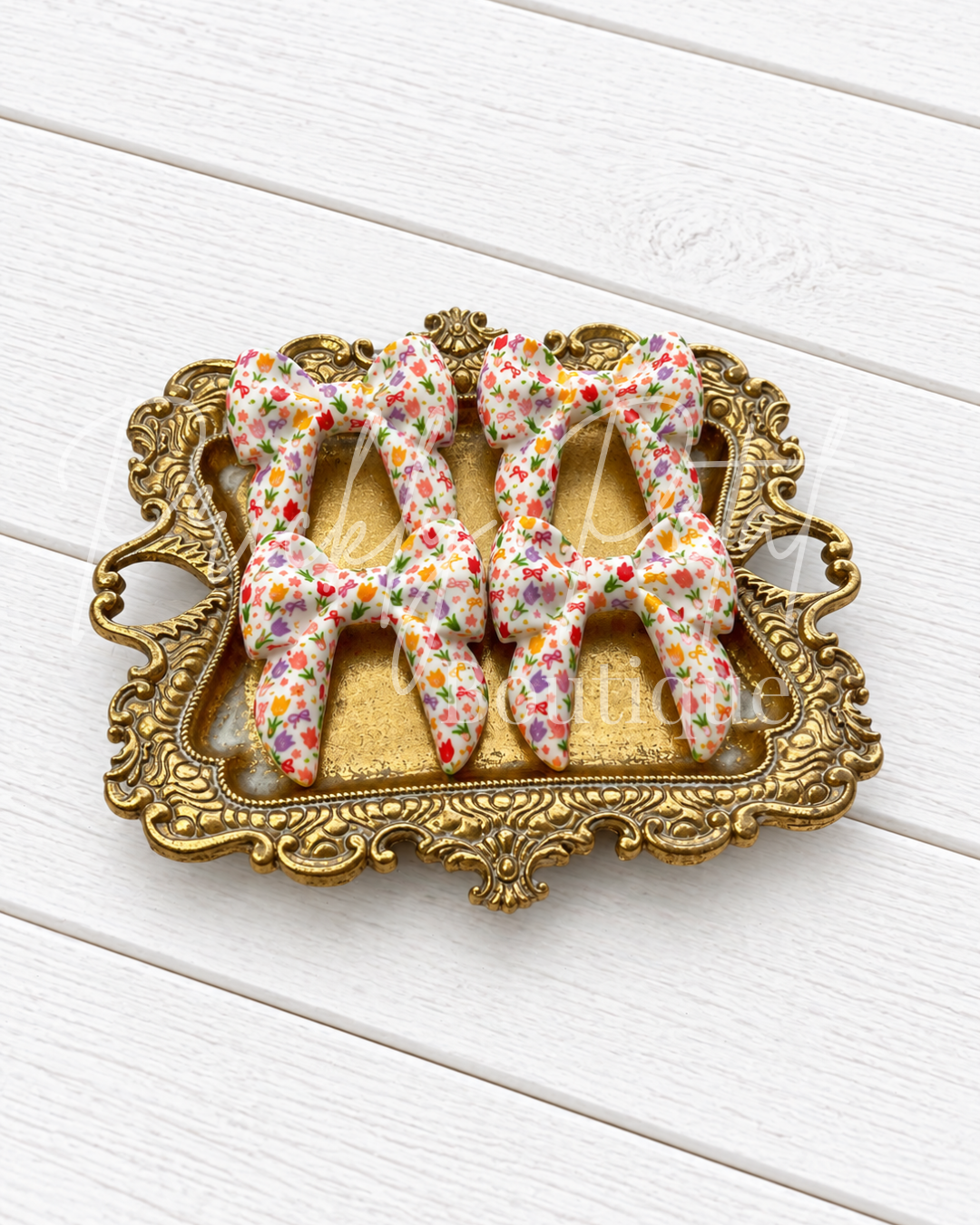 Three silicone bows displayed on an ornate gold-colored tray over a white wooden background.