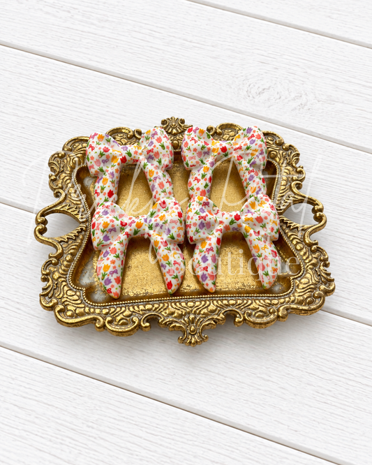 Three silicone bows displayed on an ornate gold-colored tray over a white wooden background.