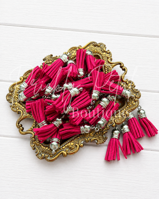 A set of bright pink velvet tassels with silver metal spacers, displayed on an ornate gold-colored tray over a white wood background.