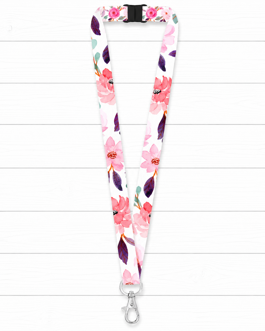 A white fabric lanyard with a pink, purple, and green watercolor floral pattern, featuring a black plastic buckle at the top and a silver metal lobster clasp at the bottom, displayed on a white wood plank background.