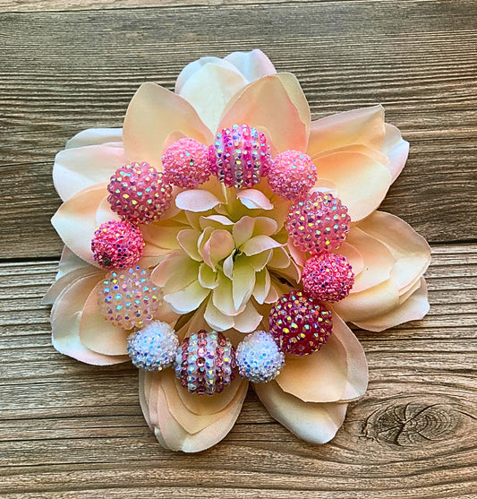A beaded bracelet with a floral design, predominantly in pink and white colors, displayed on a wooden surface.