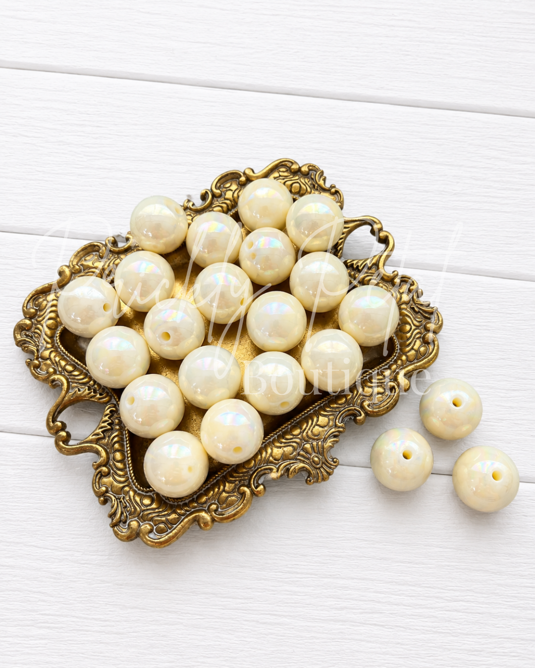 Round cream-colored craft beads with iridescent highlights, displayed in an ornate gold-colored metal dish on a white wood background.