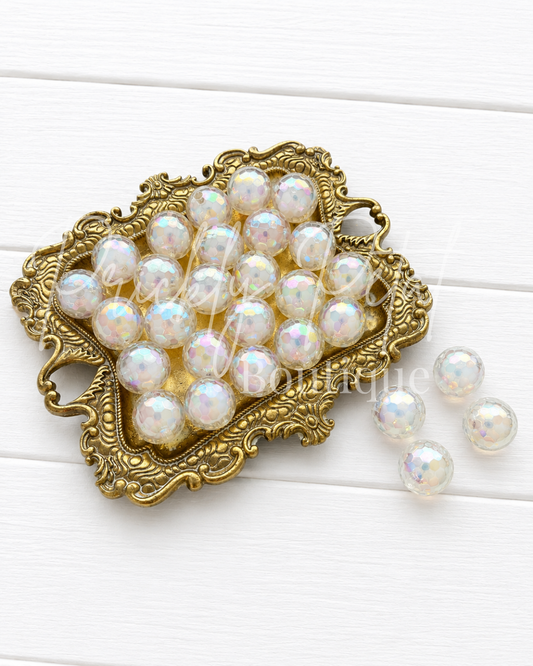 White iridescent pearl beads arranged in an ornate gold metal dish on a white wood background, with three beads placed to the right. 