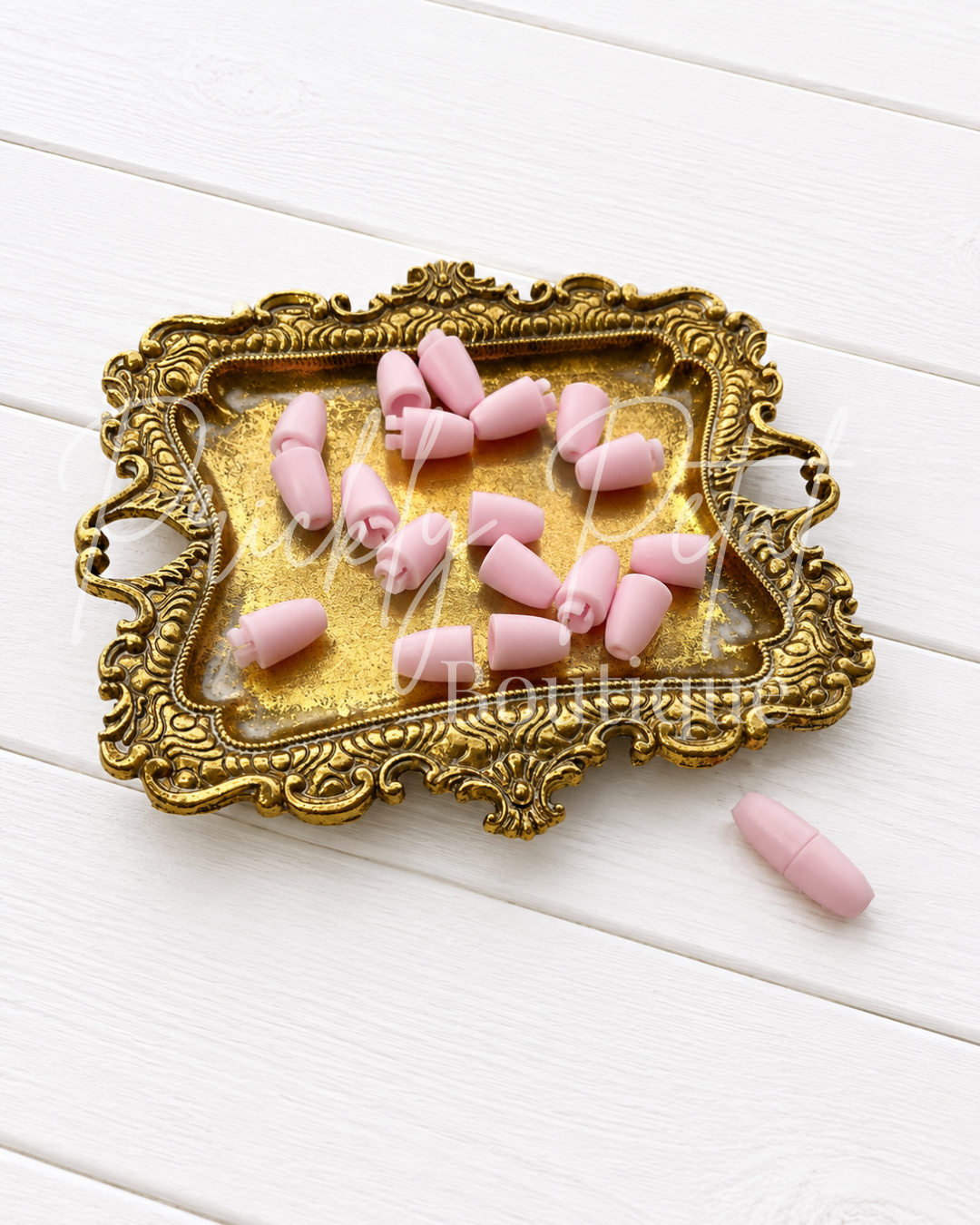 light pink breakaway lanyard clasps on gold tray against white wood background