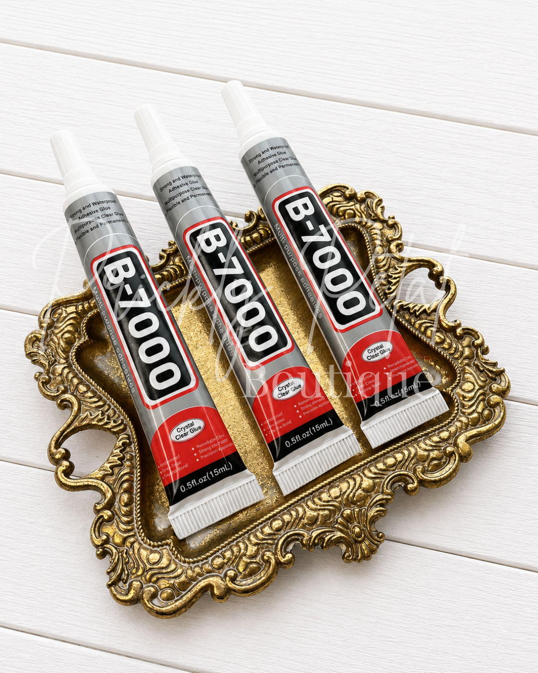Three tubes of B-7000 super glue arranged in an ornate gold tray on a white wood background.